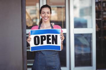 Woman holding an open sign outside of business